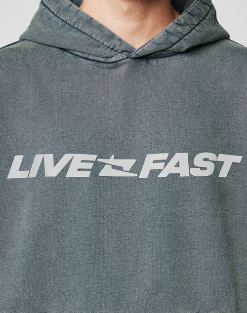A person in the LFDY Window Hooded by LIVE FAST DIE YOUNG, an oversize faded green hoodie with a reflective LIVE FAST print on the chest; their face is partially visible at the top.