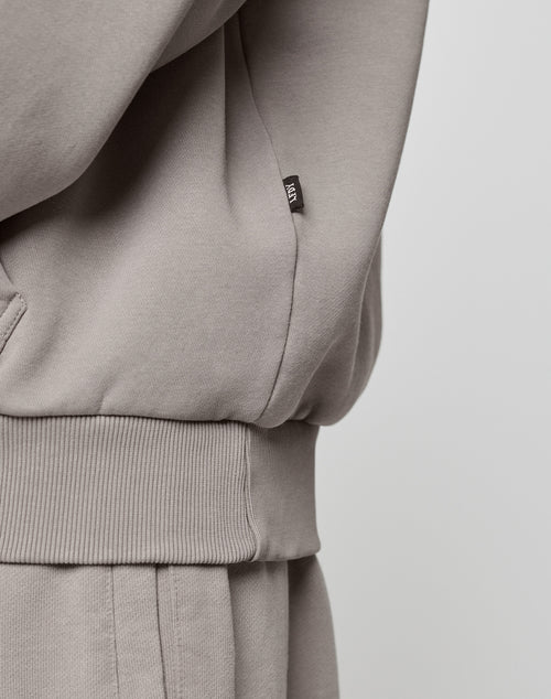 Close-up of a person wearing the LIVE FAST DIE YOUNG Basic Blank Hooded set in light gray with ribbed texture, showing a side pocket and small black tag on the sweatshirt’s seam. The background is plain and light colored.