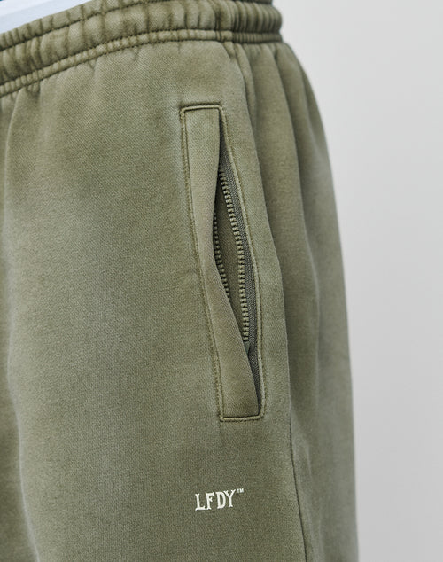 Close-up of LIVE FAST DIE YOUNGs Basic Loose Jogger in olive green, featuring a relaxed fit, zipper pocket, soft fabric with white LFDY™ embroidery near the pocket, visible stitching on the elastic waistband, and subtle logo print details.