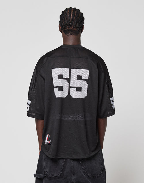 A person with braided hair is seen from behind wearing the LFDY Mesh Jersey by LIVE FAST DIE YOUNG, featuring a loose oversize fit, black mesh fabric, V-ausschnitt, and bold white "55" on back and sleeves, paired with dark shorts against a plain background.