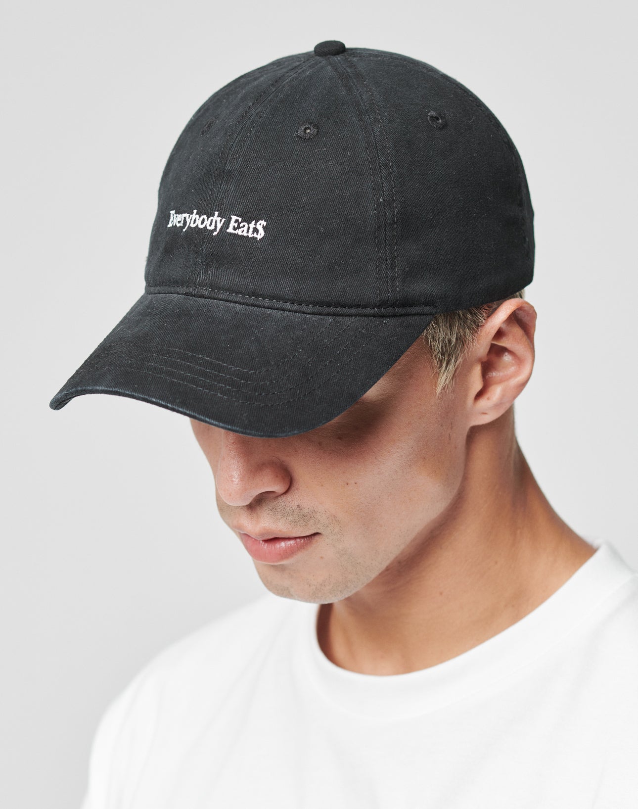 A person wears the LIVE FAST DIE YOUNG Everybody Eats Cap in black, with Everybody Eats embroidered on the front, made of Baumwolle, paired with a plain white t-shirt against a light background.