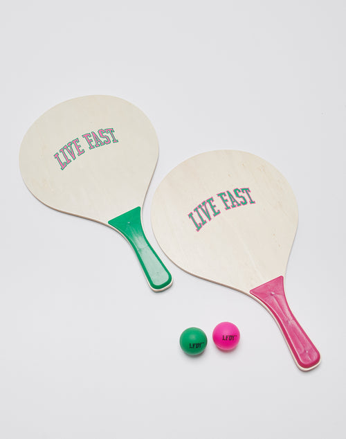 Two LIVE FAST DIE YOUNG Holzschläger, one with a green handle and one with a pink handle, and matching Live Fast Beachball Sets labeled LF/DF are displayed on a white background.
