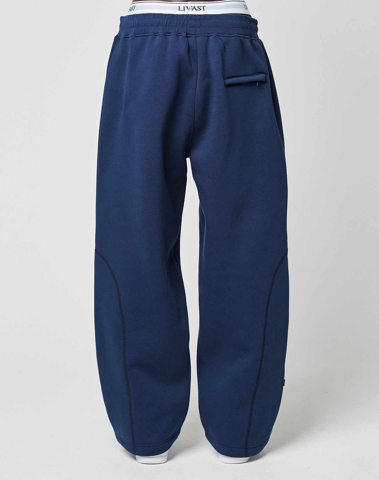 A person wearing the LFDY Active Fleece Jogger by LIVE FAST DIE YOUNG in wide fit navy blue with black stitching, a small zip pocket on the upper right, and a subtle logo print, stands against a plain light background.