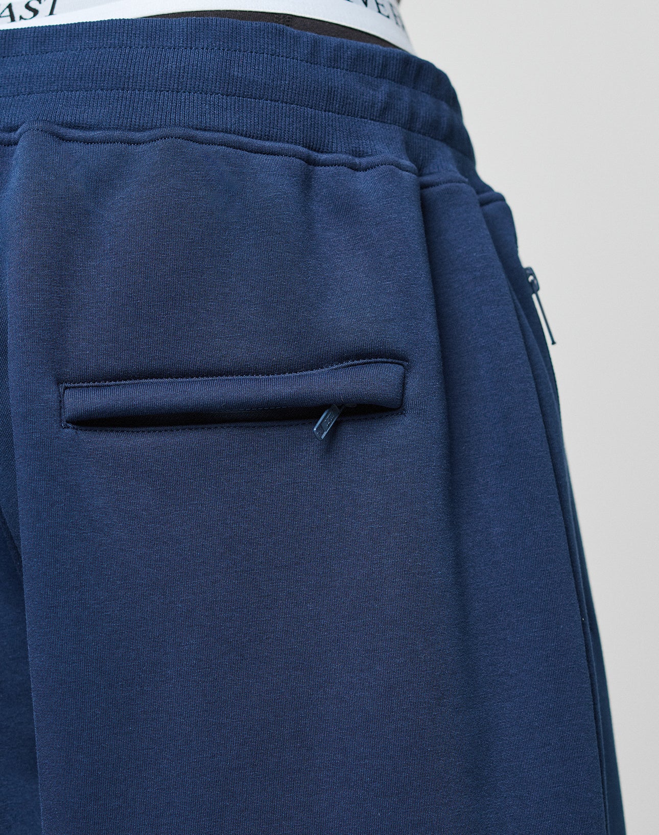 Close-up of a person wearing navy blue LFDY Active Fleece Jogger by LIVE FAST DIE YOUNG, featuring an elastic waistband and Reißverschluss Taschen. The waistband of white underwear is visible above the pants.
