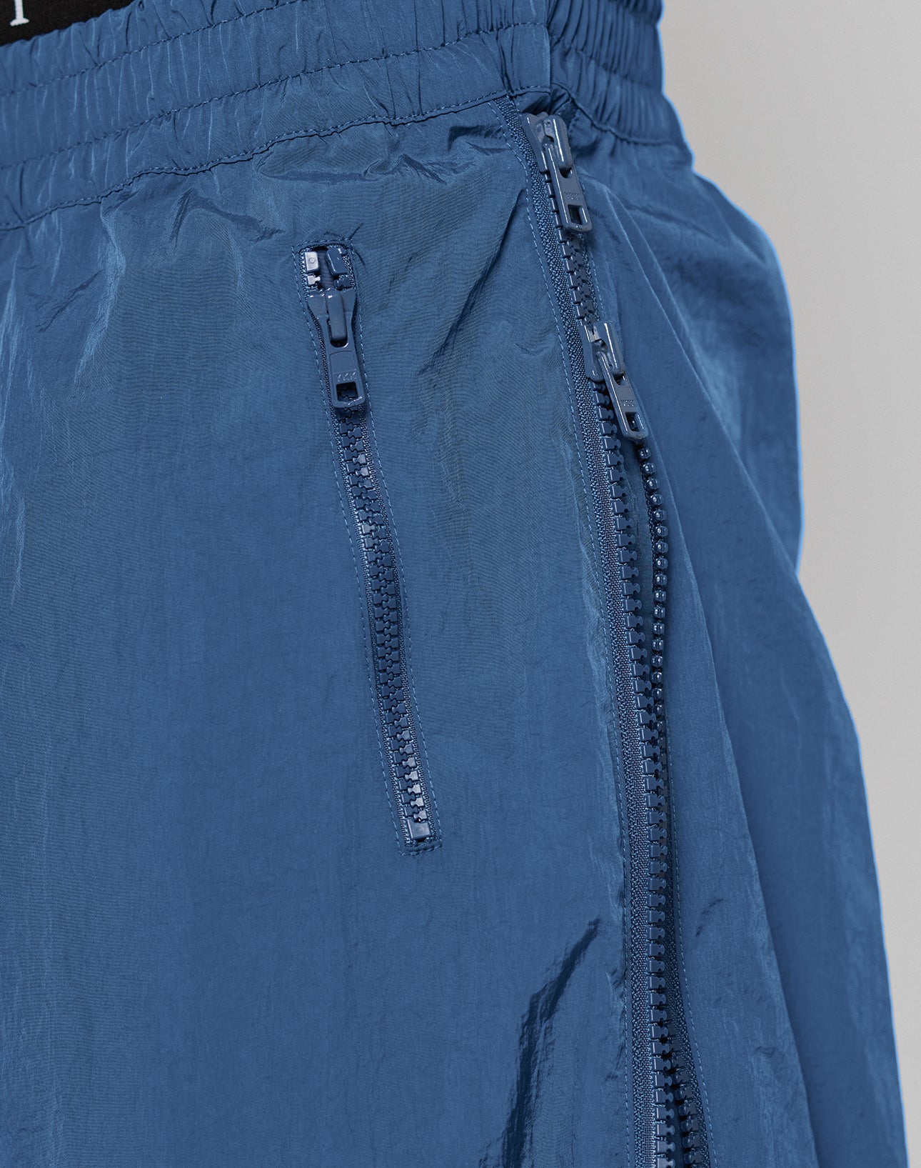 Close-up of blue Zip Tape Track Pants by LIVE FAST DIE YOUNG, Regular Fit, with two vertical Zwei-Wege Reißverschluss pockets featuring dark blue zippers and an elastischer Bund.