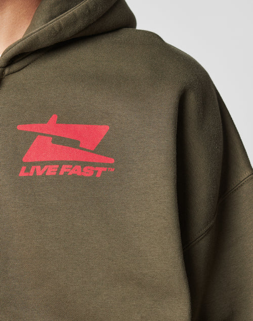 Close-up of a person in the Live Fast Sweatsuit Jacket by LIVE FAST DIE YOUNG, featuring an olive green Oversize Fit, bold red airplane graphic, and LIVE FAST text on the chest. Made from soft Baumwolle for all-day comfort.