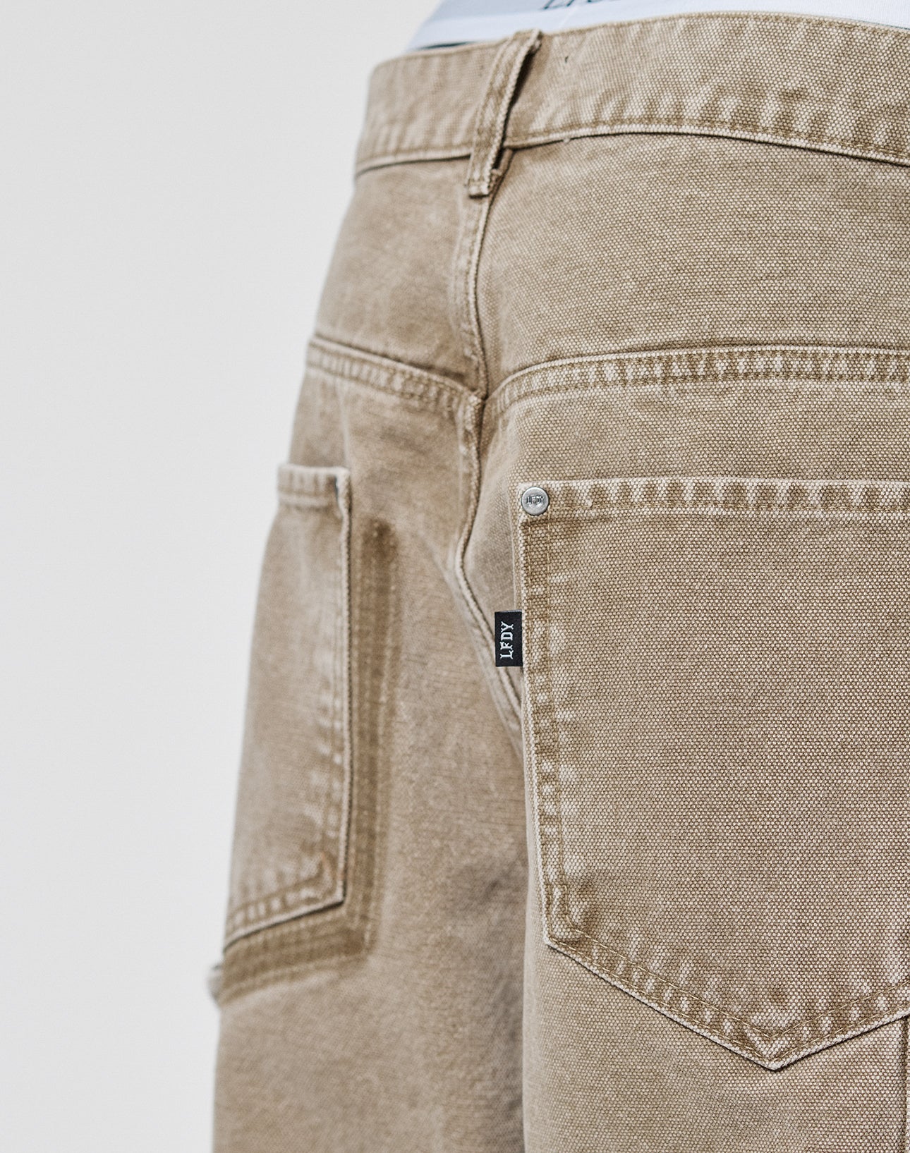 Close-up of the back of a person wearing LIVE FAST DIE YOUNG Faded Carpenter Pants in a baggy fit, featuring back pockets and a small black “ARTY” label. The background is plain and light-colored.