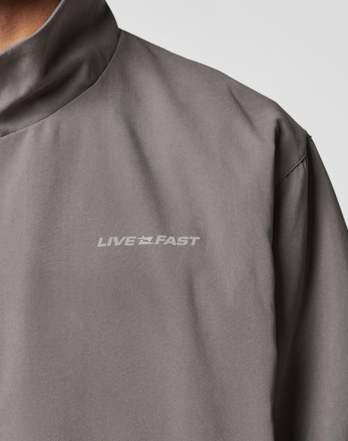 Close-up of the gray LFDY Trackjacket by LIVE FAST DIE YOUNG, featuring an oversize fit, high collar, smooth polyester fabric, and LIVE FAST in white reflective print on the chest.