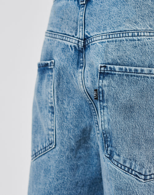 Close-up of the back of a person wearing LFDY Baggy Denim by LIVE FAST DIE YOUNG in light blue, featuring a baggy fit with wide straight legs, two back pockets, and a small black fabric tag on the right pocket.