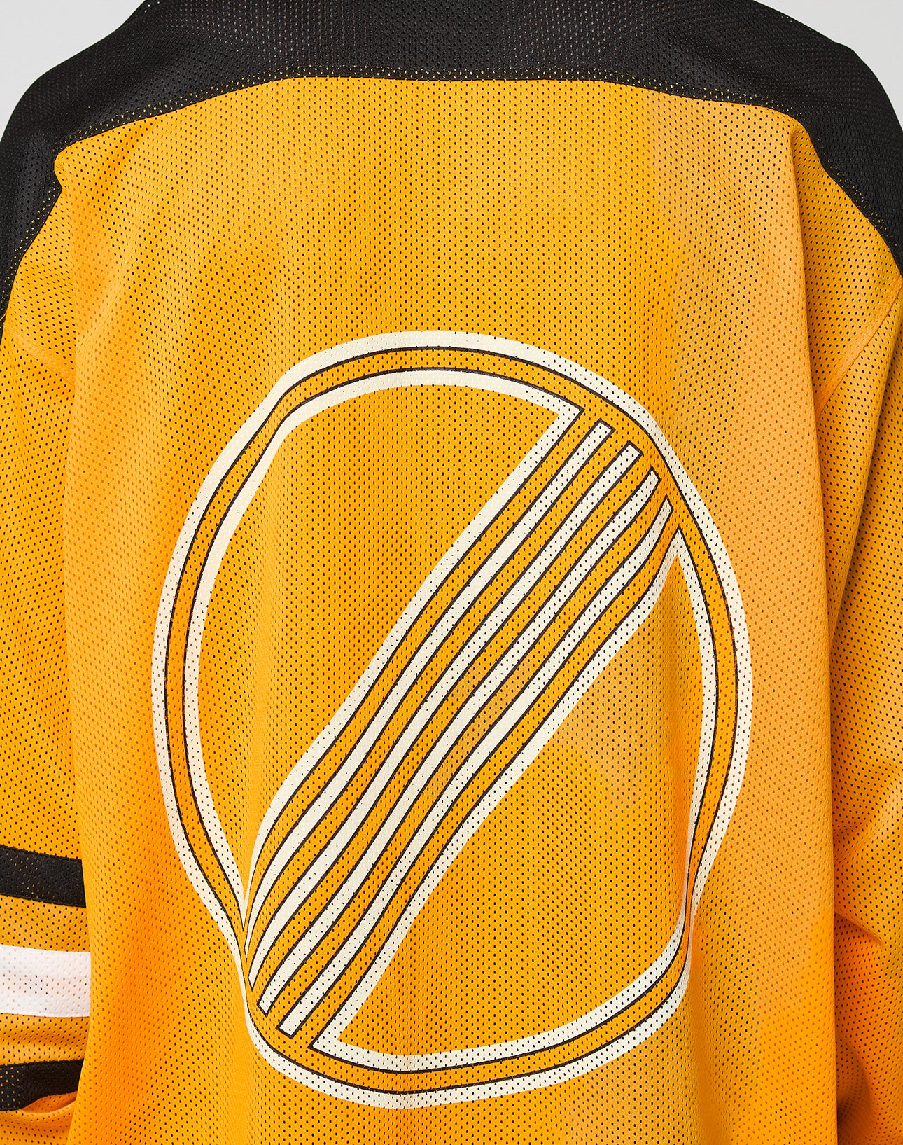 Someone wears the LFDY Autobahn Jersey by LIVE FAST DIE YOUNG—an oversized yellow mesh polyester sports top with black shoulders, striped sleeves, and a large circular white and black multilogo graphic on the back.
