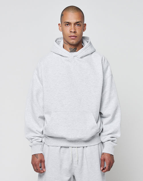 A person with a shaved head models the LIVE FAST DIE YOUNG Basic Blank Hooded and matching sweatpants in light gray, featuring an oversize fit and soft Baumwolle fabric, standing forward against a plain background.