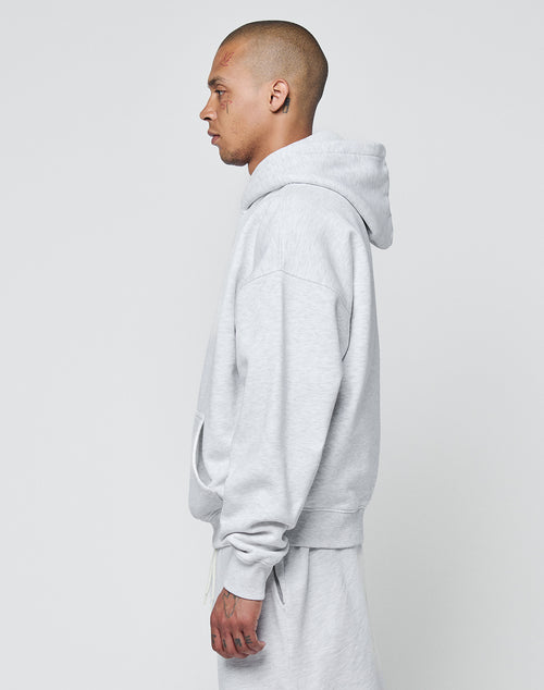 A person with closely shaved hair stands in profile, wearing LIVE FAST DIE YOUNG’s Basic Blank Hooded and matching sweatpants in a soft cotton blend, both oversize fit and light gray, against a plain light gray background.