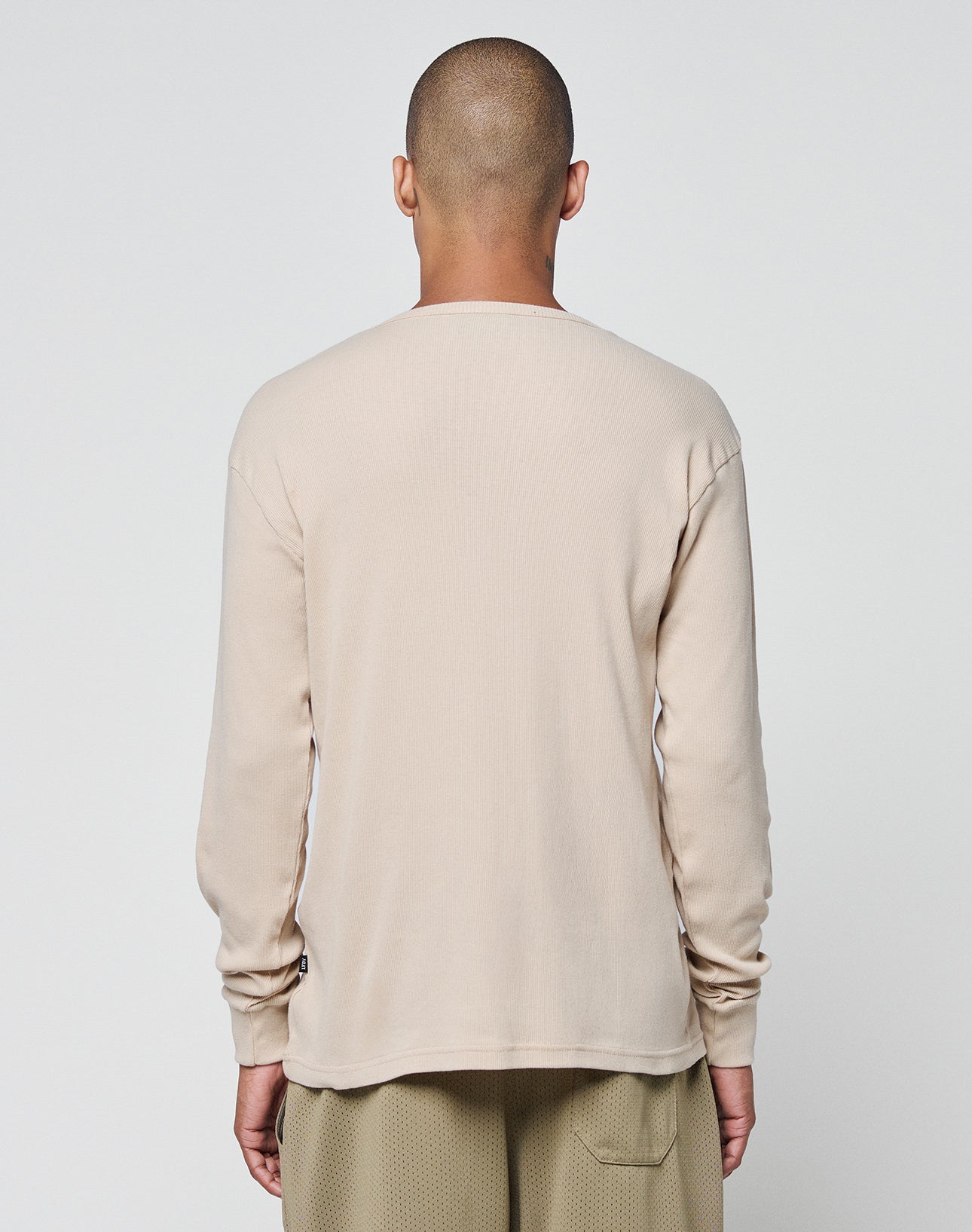 A person with a shaved head stands facing away, wearing the LIVE FAST DIE YOUNG Basic Regular Rib Longsleeve and light brown Regular Fit pants against a plain white background.