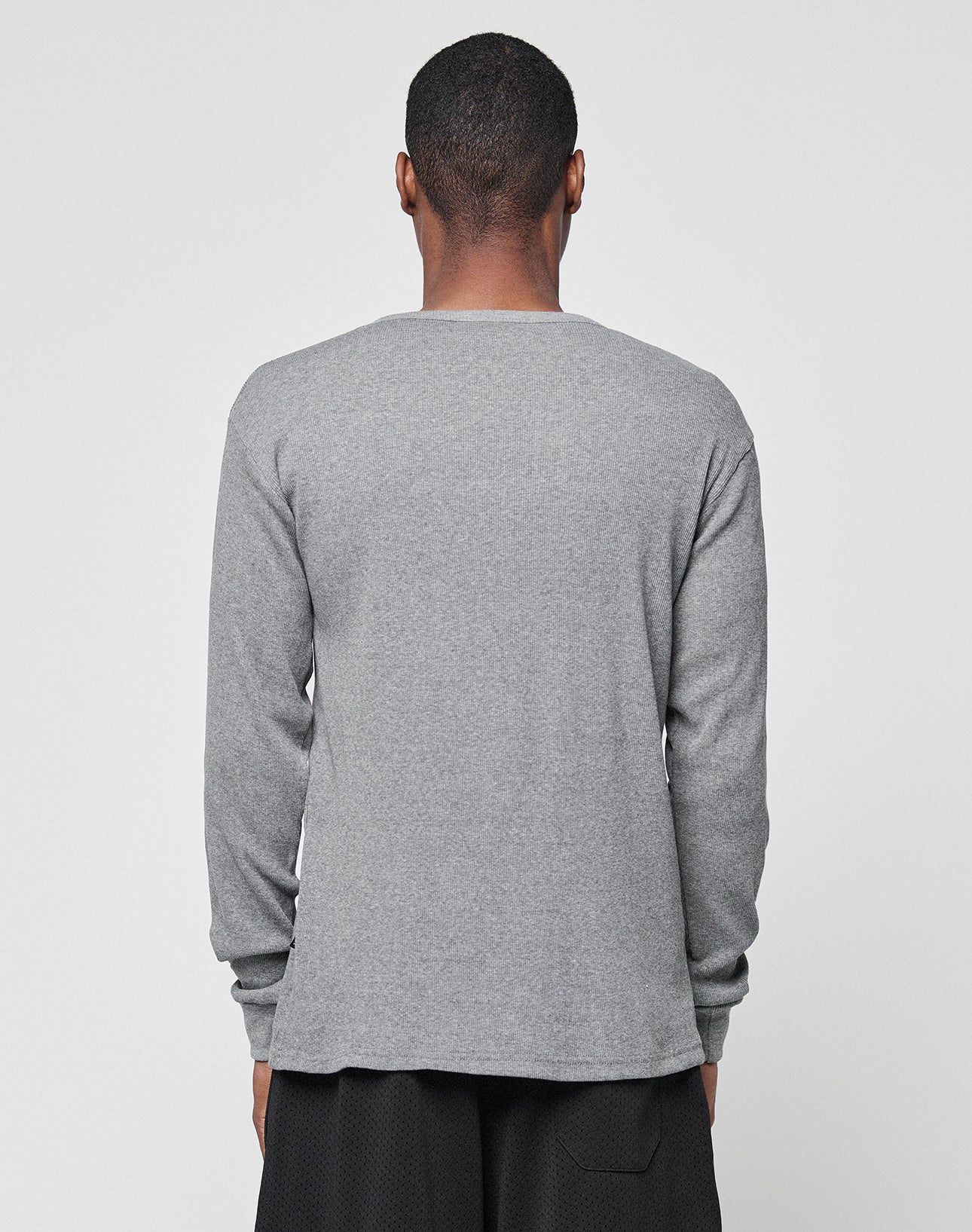 A person faces away from the camera, dressed in a gray Basic Regular Rib Longsleeve by LIVE FAST DIE YOUNG and black shorts, set against a plain light gray background.