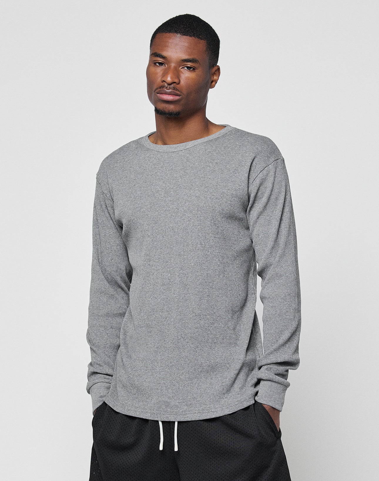 A man wears the LIVE FAST DIE YOUNG Basic Regular Rib Longsleeve, a plain gray long-sleeved shirt in Regular Fit, paired with black shorts with white drawstrings, standing against a light gray background and facing the camera.