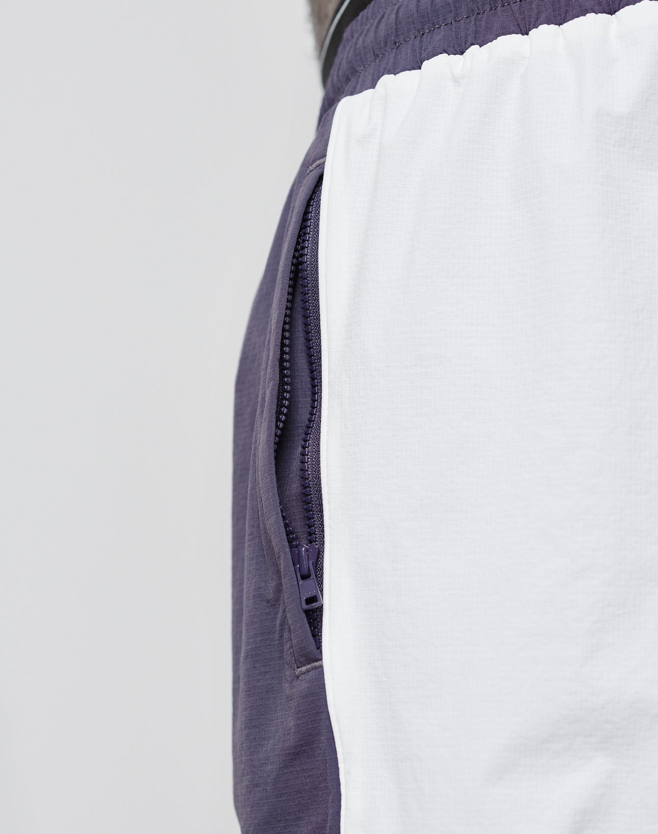 Close-up of the LIVE FAST DIE YOUNG Basic Nylon Trackshorts, showing purple fabric, a zipper pocket, white panel detail, and an elastisches Bündchen for enhanced comfort.