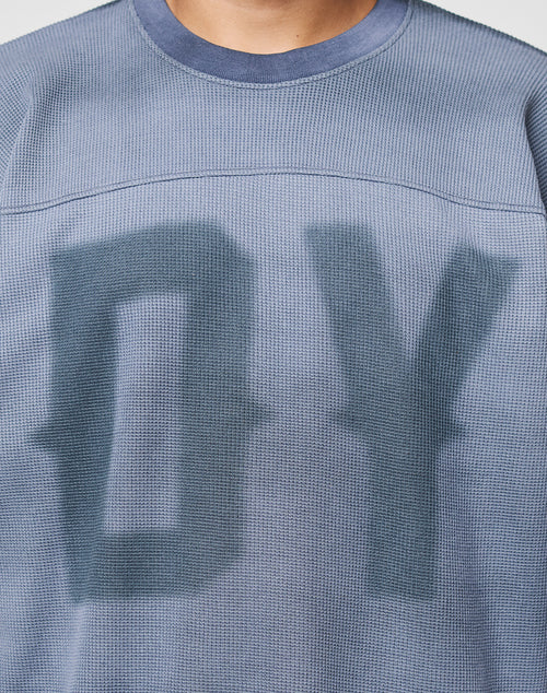 Close-up of a person wearing the LIVE FAST DIE YOUNG Faded Waffle Jersey, an oversized, textured blue shirt made from 100% Baumwolle with large blurred DY letters on the faded front; only neck and upper torso are shown.