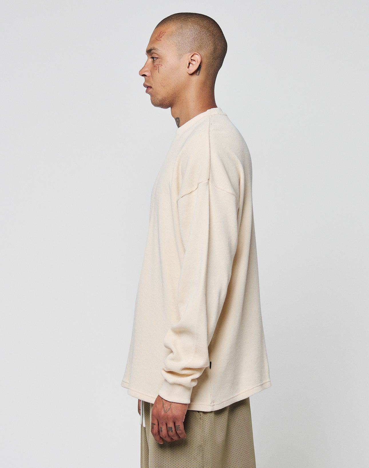 A person with a shaved head, wearing the LIVE FAST DIE YOUNG Blank Waffle Longsleeve and matching beige 100% Baumwolle pants, stands in profile against a plain white background.