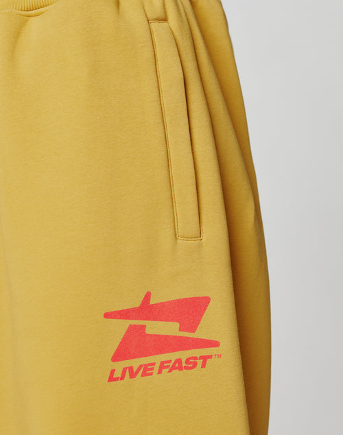 The Live Fast Sweatsuit Jogger by LIVE FAST DIE YOUNG features yellow fabric, a side pocket, elastic waistband, and a red graphic logo with LIVE FAST printed near the thigh.