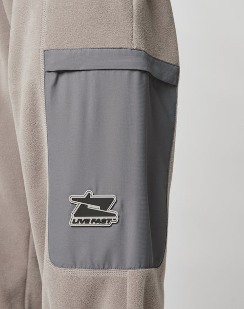 Close-up of LIVE FAST DIE YOUNG’s Live Fast Fleece Pants in gray, featuring a darker gray rectangular nylon pocket with a black and white LIVE FAST patch and a wide fit for added style.