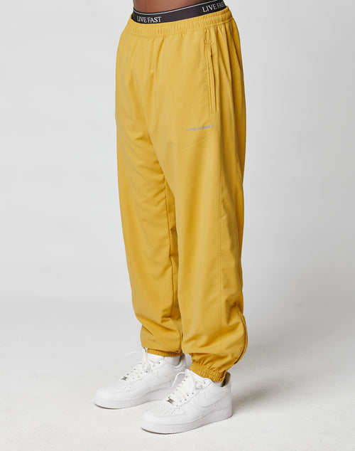 A person wearing LFDY Trackpants by LIVE FAST DIE YOUNG, featuring an elastic waistband with LIVE FAST lettering and elastic cuffs, made from soft polyester, paired with white Nike sneakers against a plain white background.