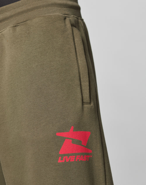 Close-up of the LIVE FAST DIE YOUNG Live Fast Sweatsuit Jogger in olive green, featuring an Oversize Fit, side pocket, wide elastic waistband, and a red LIVE FAST graphic logo and text on the upper thigh.