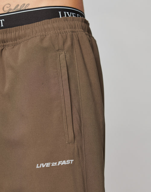 Close-up of a person wearing LFDY Trackpants by LIVE FAST DIE YOUNG with an elastic waistband, pocket, and LIVE FAST in reflective print; the black underwear’s LIVE branding is visible above the pants.