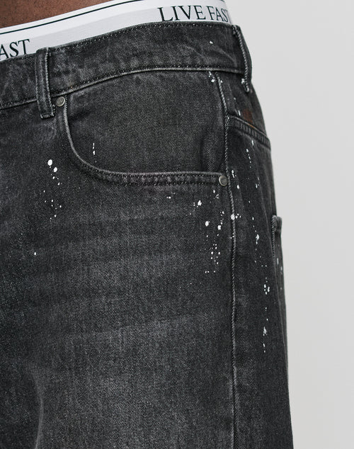 Close-up of a person wearing LFDY Baggy Denim by LIVE FAST DIE YOUNG, featuring individuelle Farbspritzer, with a visible white waistband that reads LIVE FAST in black letters.