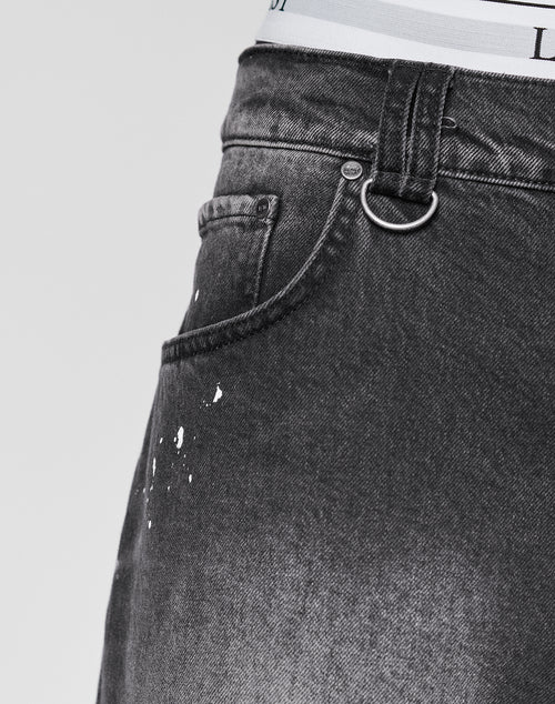 Close-up of a person wearing LIVE FAST DIE YOUNG Carpenter Jorts in dark gray, Baggy Fit, with paint splatter near the front pocket, a silver keyring on the belt loop, and white underwear waistband visible above the shorts.