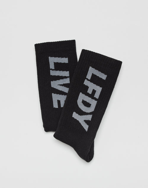 The LIVE FAST DIE YOUNG Basic Typo Socks (2 Pack) features two black cotton socks with bold gray logo text—one reads LFDY, the other LIVE—displayed on a plain white background.
