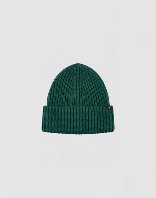 A LIVE FAST DIE YOUNG Rib Knit Beanie in green, featuring a folded brim with a small rectangular flag label, is centered on a plain light gray background.
