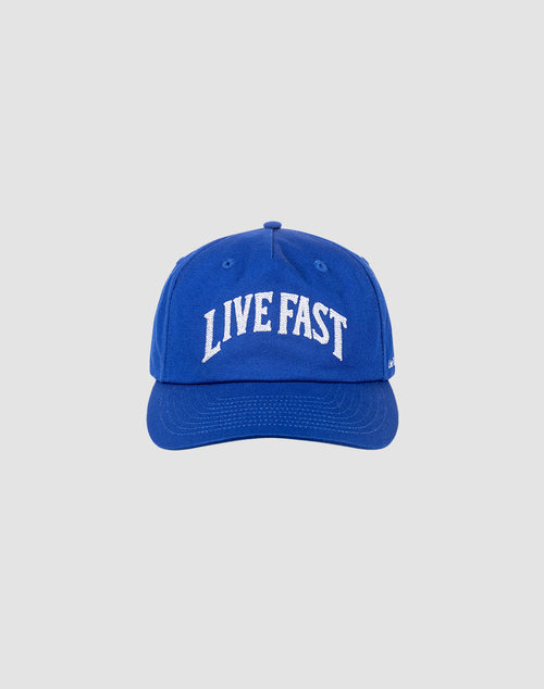 The Live Fast Unstructured Cap by LIVE FAST DIE YOUNG is a blue baseball cap with LIVE FAST in bold white letters on the front and a Flag-Label on the side, displayed against a plain light gray background.