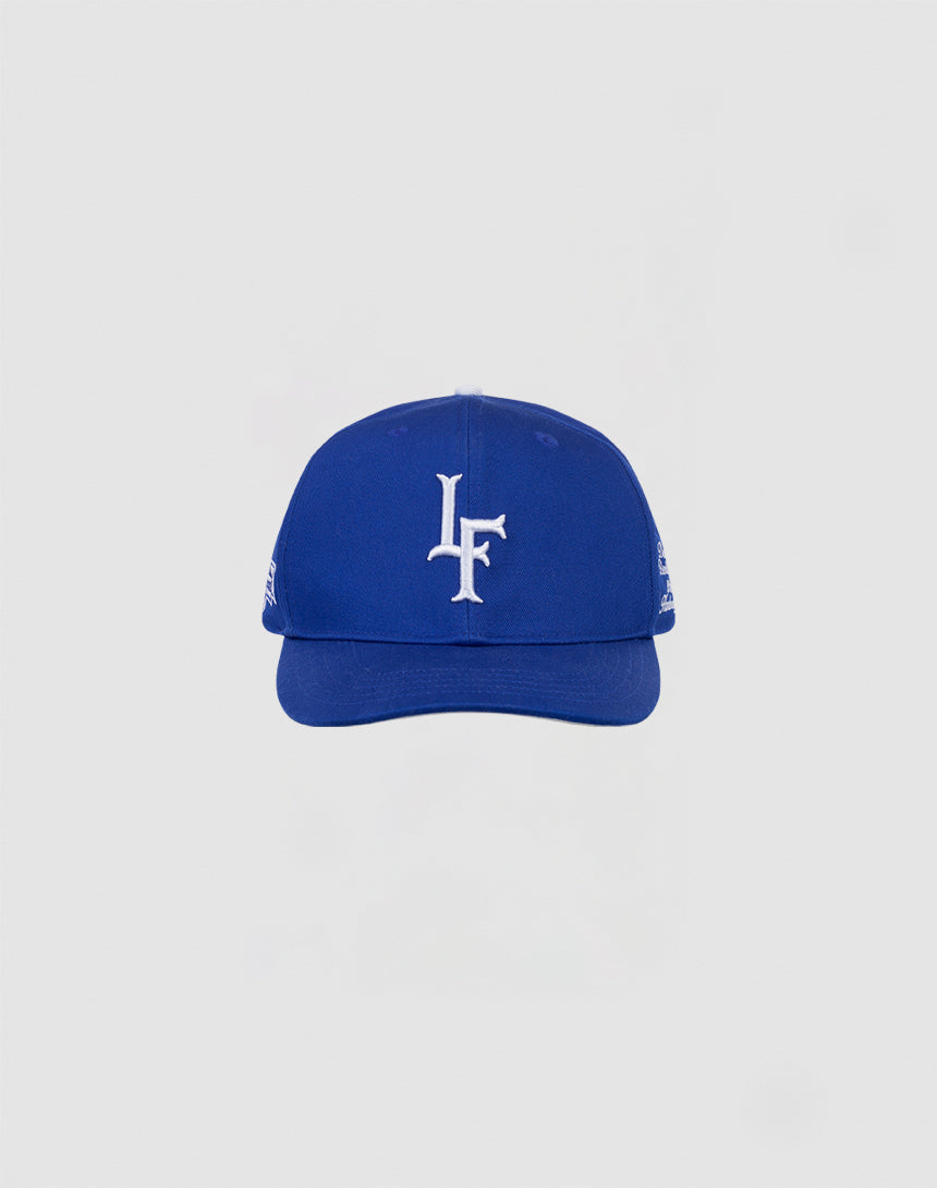 The LF 10th Snapback by LIVE FAST DIE YOUNG is a blue 100% cotton baseball cap with a white LF Multi-Logo embroidered on the front, shown on a light gray background. Features an adjustable snap closure.