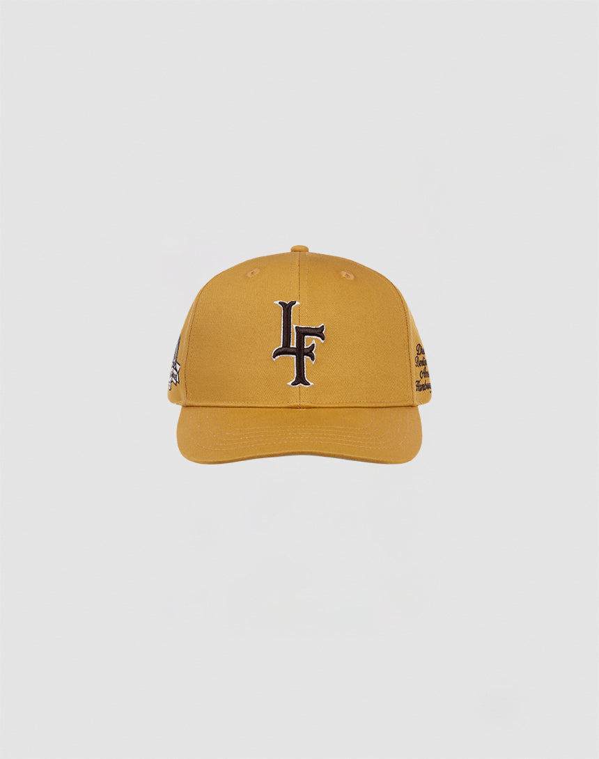 The LF 10th Snapback by LIVE FAST DIE YOUNG is a mustard yellow cotton baseball cap with a black and white LF logo on the front and a snap closure, shown against a plain white background.