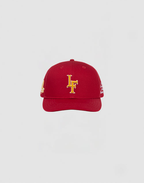 The LIVE FAST DIE YOUNG LF 10th Snapback is a red baseball cap with a yellow embroidered LF logo, made from 100% Baumwolle and designed with a Mit Snapverschluss, shown on a plain light gray background.