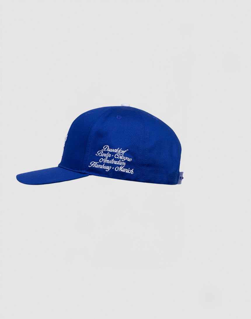 The LF 10th Snapback by LIVE FAST DIE YOUNG, made from 100% Baumwolle in royal blue, is shown in profile on a light gray background. White cursive Multi-Logo Stick embroidery decorates the side with multiple words or names.