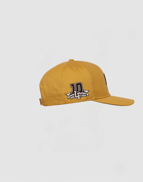 The LF 10th Snapback by LIVE FAST DIE YOUNG features mustard yellow Baumwolle fabric, a 10 Doomsday 2006 embroidered patch, and Multi-Logo side detailing, displayed on a plain white background.