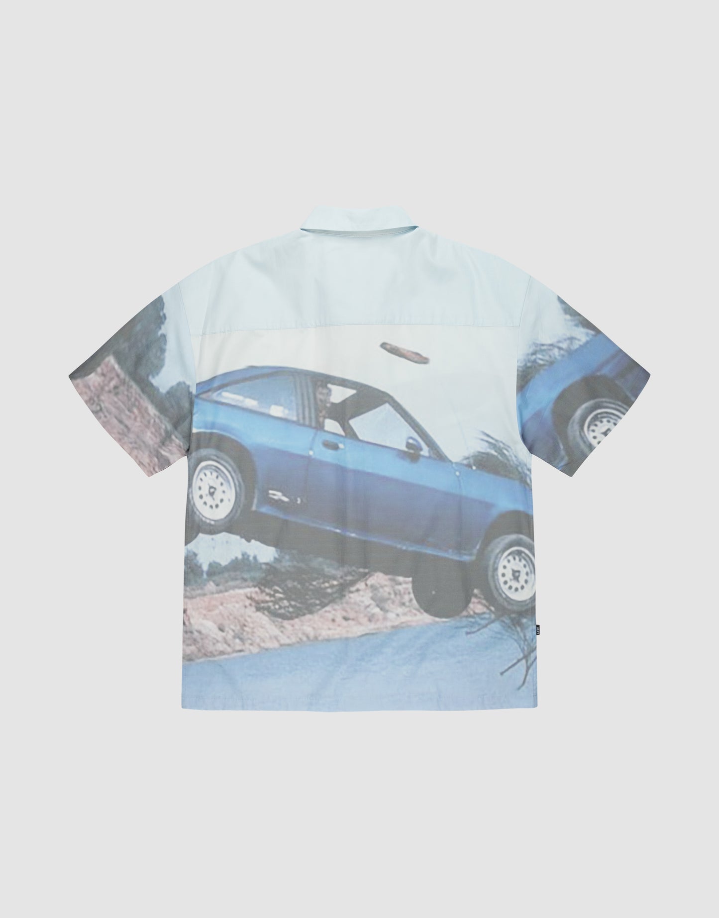 The LFDY Crash Kid Shirt by LIVE FAST DIE YOUNG is a short-sleeve, oversized print shirt featuring an airborne blue car on a dirt road with a light blue and white background and subtle logo details for a stylish touch.