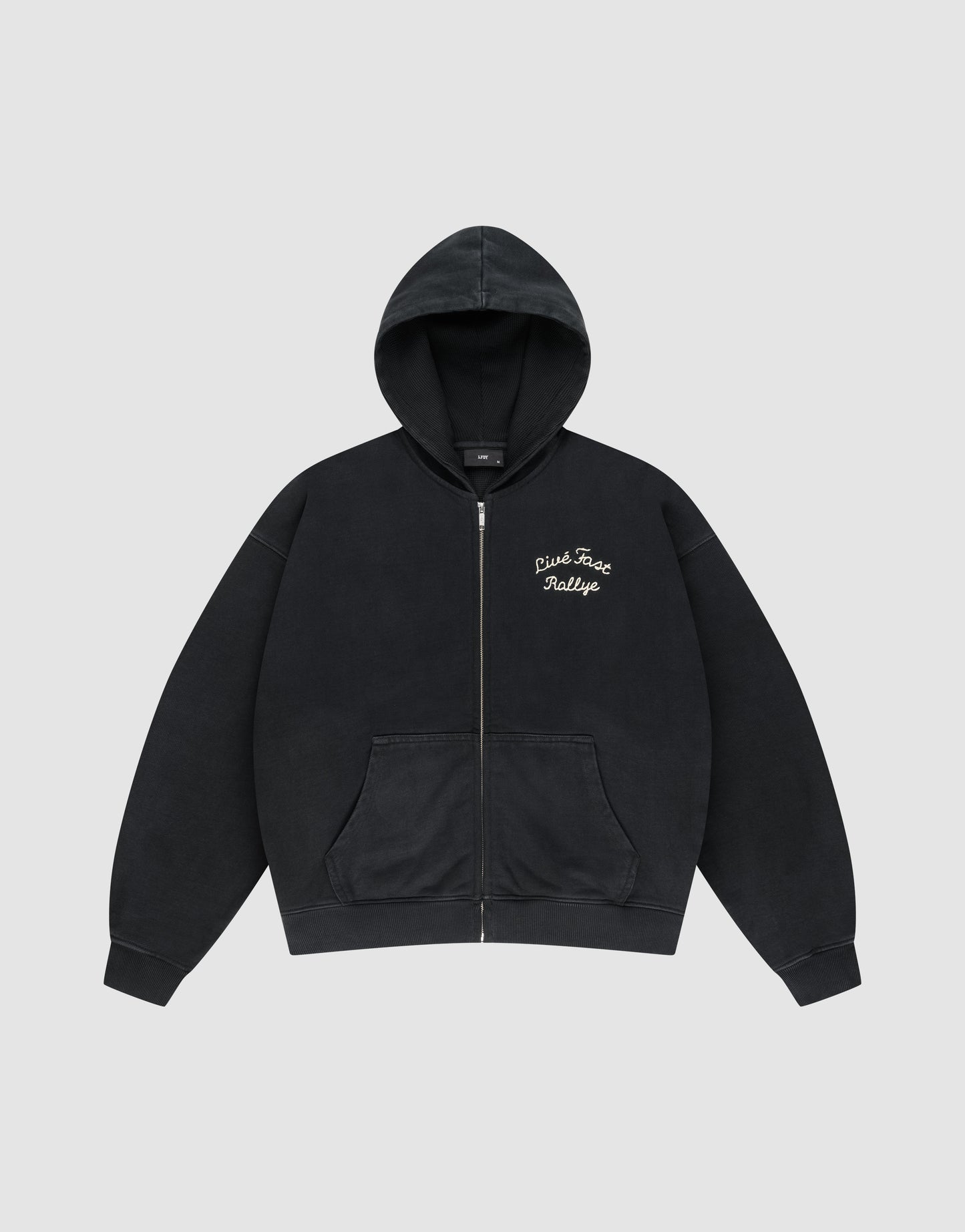 The LFDY L’Équipe Hooded Zip by LIVE FAST DIE YOUNG is a black oversized hoodie with a front pocket, hood, cozy waffle innenfutter, and white embroidered "Pink Face Rallye" text on the left chest. Laid flat on light gray background.