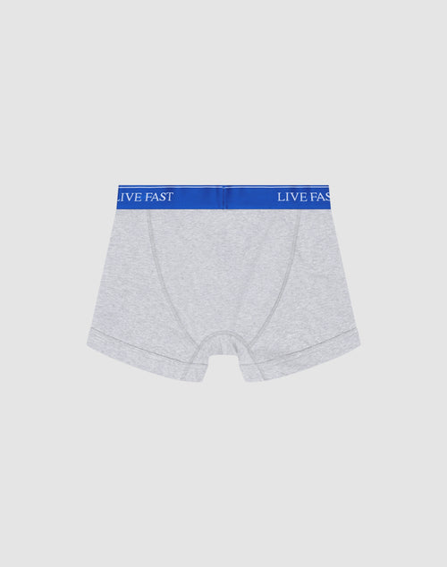A pair of light gray Live Fast Trunks by LIVE FAST DIE YOUNG in Regular Fit, made of soft cotton with a blue elastic waistband reading LIVE FAST in white, shown on a plain white background.