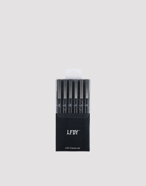A black box labeled LIVE FAST DIE YOUNG LFDY Fineliner Set holds six wasserfest black fineliner pens with varying line widths, arranged vertically cap-up against a plain light gray background.