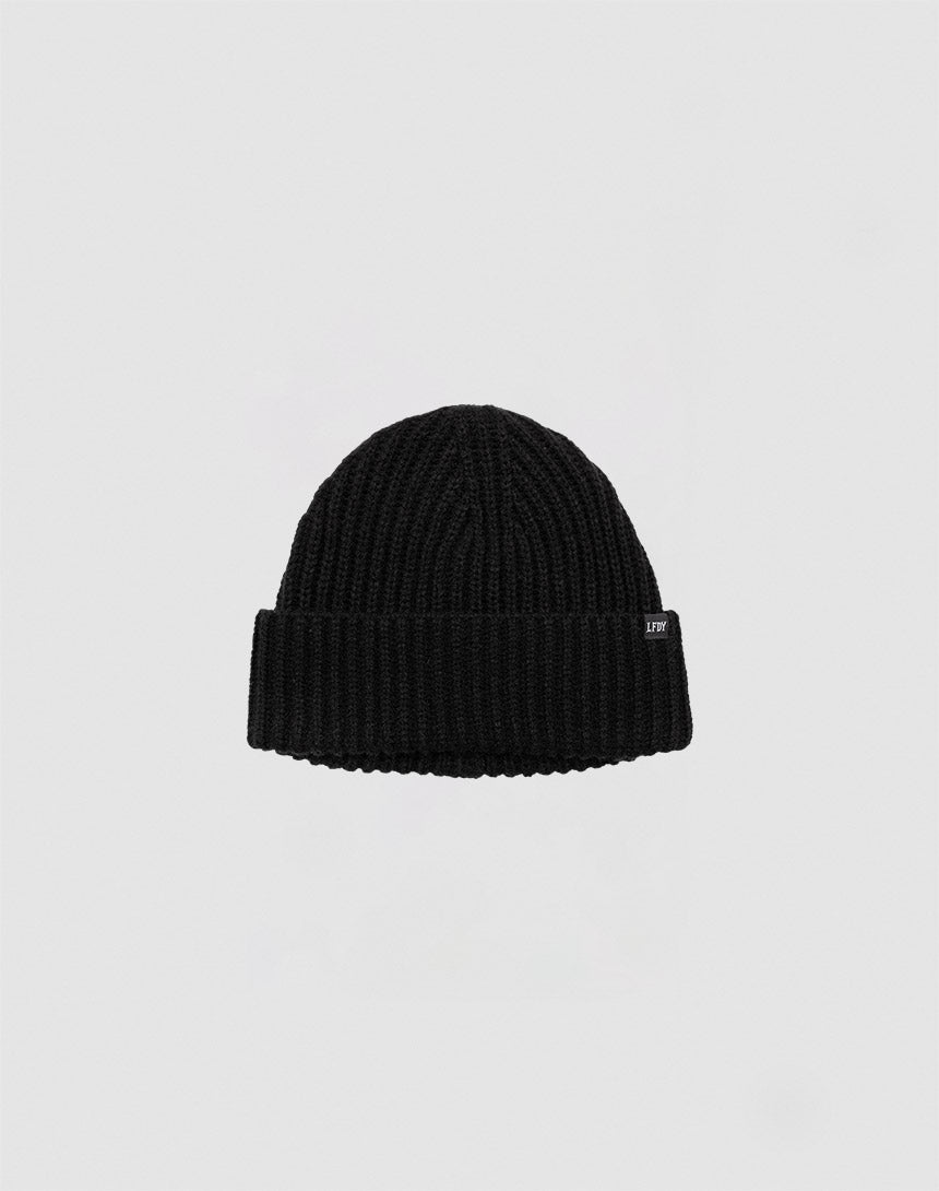 A black LFDY Rib Knit Beanie made from soft polyacryl, featuring a folded brim and a small rectangular side tag, is shown against a plain light gray background.