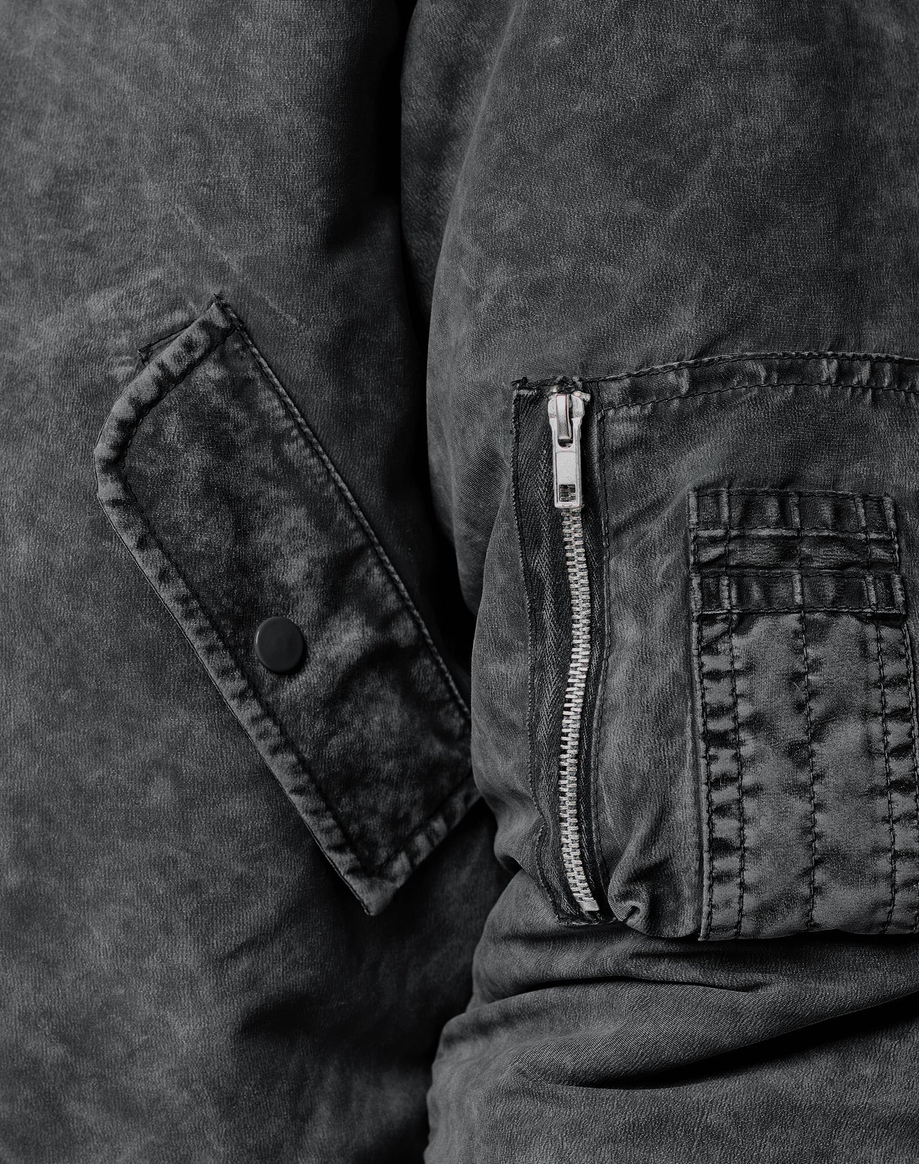 Close-up of the LIVE FAST DIE YOUNG Washed Bomber Jacket in black textured fabric, regular fit, featuring visible stitching, a vertical zipper pocket, and a flap with a black snap button.
