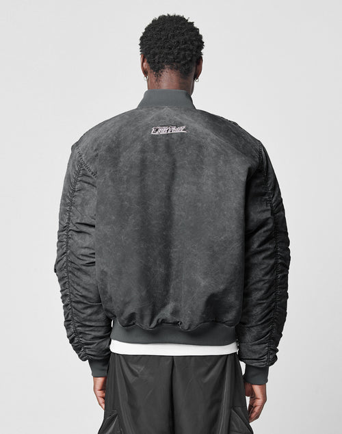 A person with short curly hair is seen from behind in LIVE FAST DIE YOUNGs Washed Bomber Jacket—regular fit, textured black with a small white upper-back logo—paired with black pants, set against a plain light gray background.