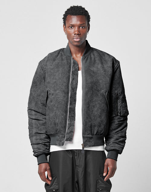 A person with short hair wears a LIVE FAST DIE YOUNG Washed Bomber Jacket over a white shirt and black pants, standing against a plain light gray background, facing forward with a neutral expression.