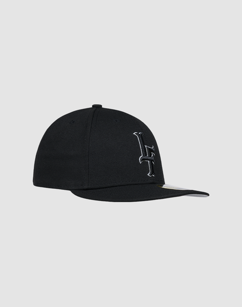 The LFDY X NEW ERA 59FIFTY Low Profile cap by LIVE FAST DIE YOUNG features a black design, curved brim, and a white embroidered L crossed by a line on the front, shown against a plain light gray background.