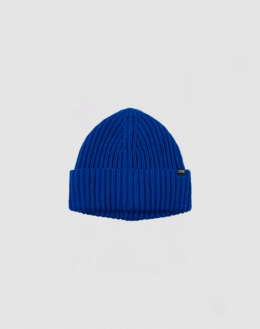 The LIVE FAST DIE YOUNG Rib Knit Beanie is a cozy blue Polyacryl hat with a folded brim, shown on a light grey background. One size for comfort and style.