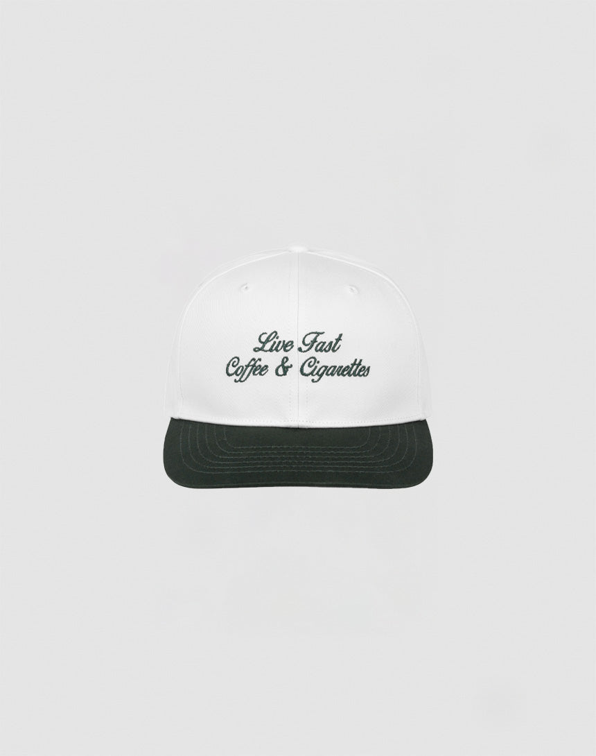 The LIVE FAST DIE YOUNG Live Fast Coffee Cap is a white, one size cap made from 100% Baumwolle with Live Fast Coffee & Cigarettes embroidered in dark green on the front, inspired by the LFDY Berlin Café and shown on a plain light gray background.