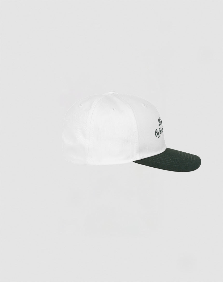 The Live Fast Coffee Cap by LIVE FAST DIE YOUNG is shown in side view against a light gray background. This white 100% cotton cap has a dark green brim, Berlin Café style branding, and comes in one size.