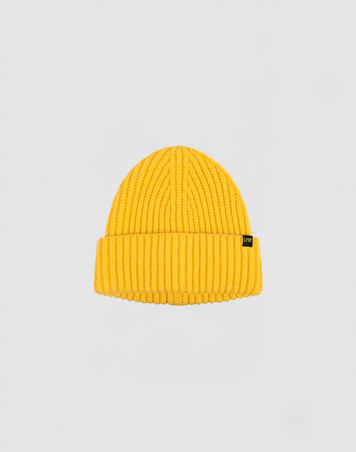 A yellow LIVE FAST DIE YOUNG Rib Knit Beanie, made from cotton with a folded brim and a small black side tag, is shown on a plain light gray background.